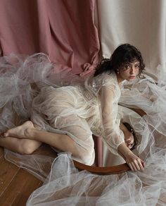 a woman laying on top of a wooden floor next to a pink curtain and chair