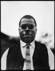 a black and white photo of a man with sunglasses on his head wearing a vest and tie