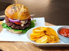 a hamburger and fries on a white plate with dipping sauce next to it, sitting on a wooden table