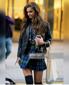 a woman in a kilt is walking down the street while looking at her cell phone