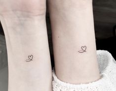 two small tattoos on the wrist that are both heart shaped and love is written in cursive letters