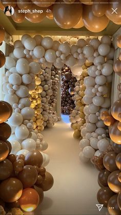 balloons are hanging from the ceiling in an open area with white and gold decorations on either side