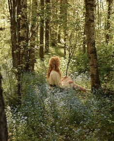 a woman is sitting in the woods surrounded by wildflowers and bluebells