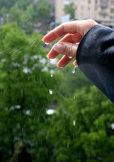 a person's hand reaching out to the rain