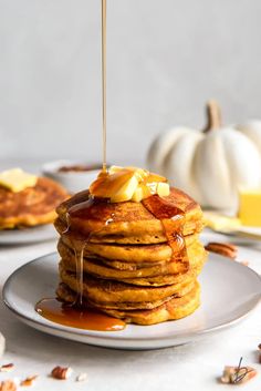 a stack of pancakes with syrup and butter on a white plate next to pumpkins