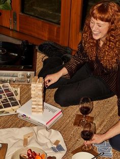 a woman sitting on the floor with some food and wine