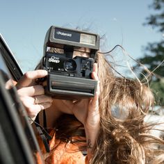 a woman holding up a camera to take a picture in the back seat of a car