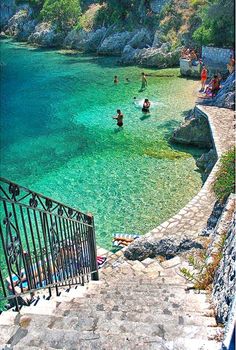 people are swimming in the clear blue water near some steps leading to an iron gate