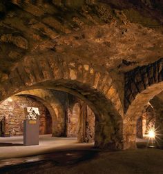 an underground passage with stone walls and arches leading into the light at the end of the tunnel