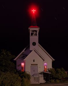 a white church with a red light on it's steeple at night time