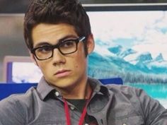 a young man wearing glasses is sitting in front of a television screen and looking at the camera