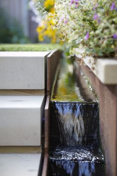 water flowing down the side of a building into a garden pond with flowers in it