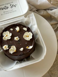 a chocolate cake with white flowers on top in a plastic container sitting on a table