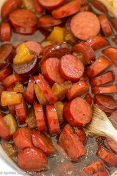 cooked sausages and potatoes in a pot with a wooden spoon