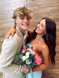 a young man and woman hugging each other in front of a wooden wall holding flowers