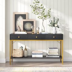 a black and gold console table with books, vases and plants on it in front of a white wall