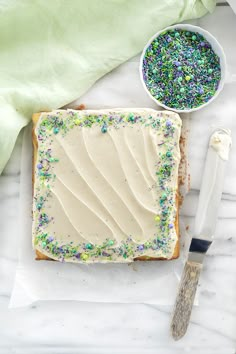 a cake with white frosting and sprinkles on it next to a knife