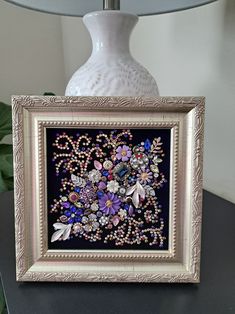 a white vase sitting on top of a black table next to a framed flower arrangement