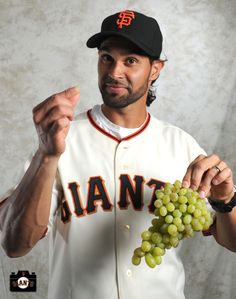 a man in a baseball uniform holding grapes