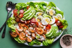 a white plate topped with lettuce covered in tomatoes and hard boiled eggs next to a fork