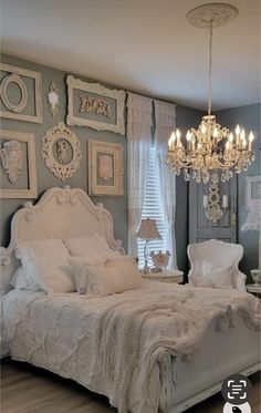 a white bed sitting under a chandelier in a bedroom next to a window