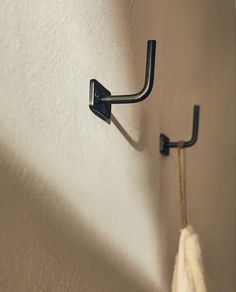 a towel hanging on the wall next to a pair of black metal hooks and a white towel