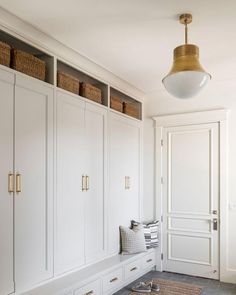 a white closet with lots of drawers and baskets on the wall next to it is lit by a pendant light