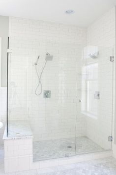 a bathroom with a walk in shower next to a white toilet and sink under a window