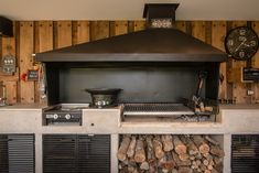 an outdoor kitchen with wood stacked on the counter and a large stove top over it