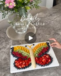 a butterfly shaped fruit platter on a table next to a vase with pink flowers