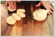 two hands are kneading dough on a wooden table