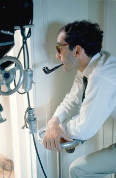 a man in white shirt and tie sitting on stool with pipe sticking out of mouth