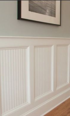 an empty room with white paneled walls and wood flooring, framed artwork on the wall