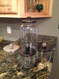 three glass jars sitting on top of a granite counter next to wooden cabinets and drawers