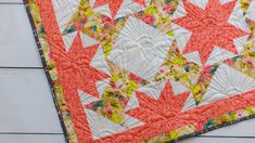 an orange and white quilt on top of a wooden table next to a pair of scissors