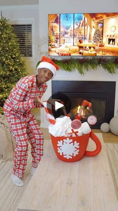 a man in plaid pajamas and santa claus hat standing next to a fire place