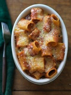 a white bowl filled with pasta on top of a wooden table next to a fork