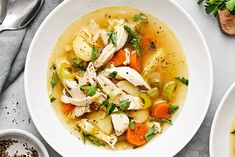 a white bowl filled with chicken and vegetable soup next to another bowl full of vegetables