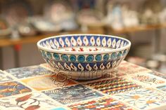 a bowl sitting on top of a table covered in colorful tiles and designs with words written below it