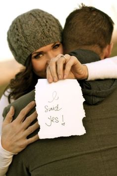 a man and woman hugging each other while holding a piece of paper that says i said yes