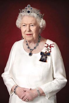 an older woman wearing a tiara and holding her hands in her pockets while standing against a red background