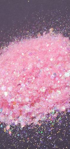 a pink substance is sprinkled with multicolored confetti on a black surface