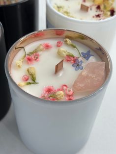 two cups filled with milk and flowers on top of a white table next to each other