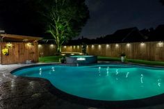 a backyard with a pool at night and some lights on the side of the pool