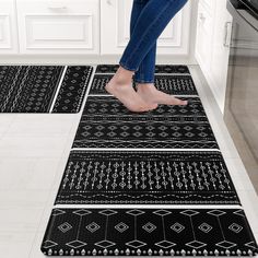 a woman standing on the kitchen floor in front of two black and white rugs