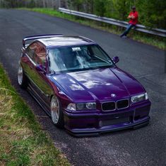 a purple car parked on the side of a road next to a person in a red shirt