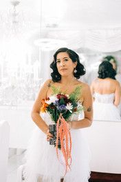 a woman standing in front of a mirror with flowers on her wedding dress and holding a bouquet