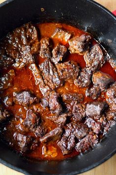 beef stew in a skillet on a wooden table with a red cloth next to it