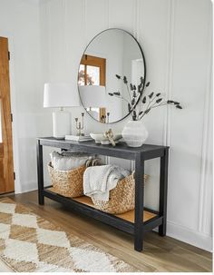 a black console table with baskets under it and a round mirror on the wall behind it