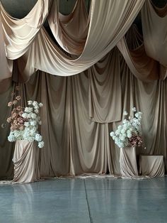 two vases filled with flowers sitting on top of a stage covered in drapes